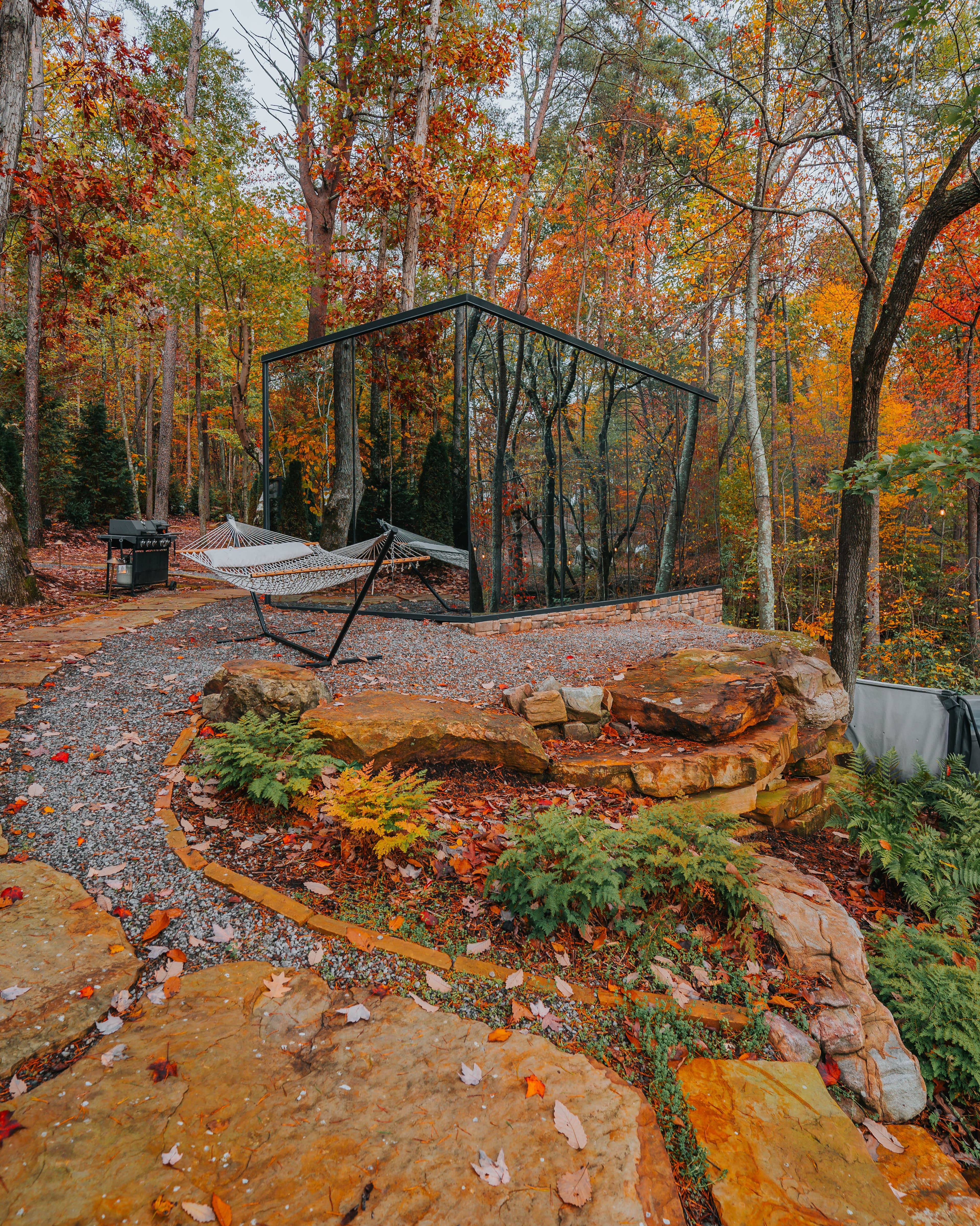 Mirror cabin surrounded by fall foliage with hammock and stone fire pit at BOLT FARM Treehouse